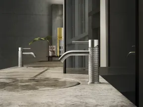 Modern bathroom sink with textured stainless steel faucet on a stone countertop with reflective dark glass backsplash.
