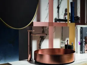 Modern bathroom countertop with a copper vessel sink, sleek faucet, marble surface, and decorative shelving with books.
