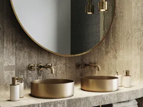 Modern bathroom with round gold sinks, wall-mounted gold faucets, large circular mirror, and hanging gold pendant lights.