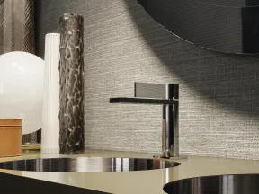 Modern bathroom countertop with dual round sinks, sleek chrome faucet, decorative vases, and textured wall.