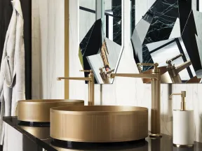 Modern bathroom with gold vessel sinks, geometric mirrors, marble walls, and black countertop with gold fixtures.