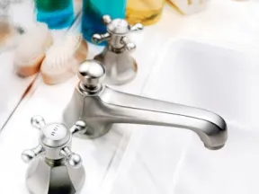Close-up of a modern silver faucet with hot and cold handles on a clean white sink countertop.