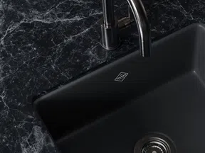Modern black kitchen sink with metallic faucet on dark marble countertop with white veins.