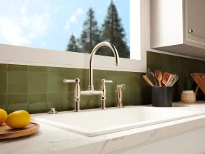 Modern kitchen sink with polished chrome faucet, green tile backsplash, and utensils in a black holder