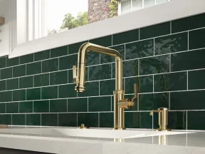 Modern kitchen sink with brass faucet and deep green subway tile backsplash under a large window.