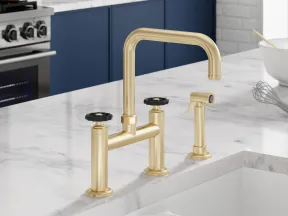 Modern kitchen faucet with gold finish on marble countertop next to stainless steel stove and blue cabinets