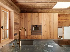 Modern kitchen with wooden walls, brass faucet, black marble countertop, built-in oven, and large window.