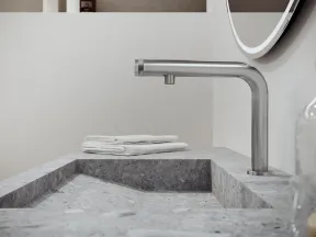 Modern bathroom sink with gray stone countertop, stainless steel faucet, and folded white towels on edge.