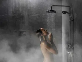 Woman enjoying a relaxing shower under a rain showerhead in a steamy modern bathroom with dark tiles.