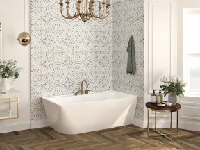 Modern bathroom with freestanding white bathtub, patterned accent wall, chandelier, and wooden herringbone floor.
