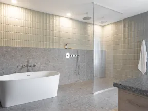 Modern bathroom with freestanding white tub, walk-in shower, textured tiles, and stone flooring.