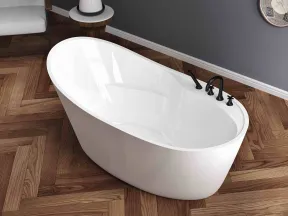 Modern white freestanding bathtub on brown herringbone wooden floor with gray wall and armchair nearby