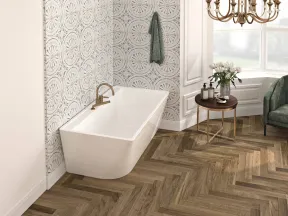 Modern bathroom with white freestanding bathtub, patterned tile wall, wooden herringbone floor, and chandelier