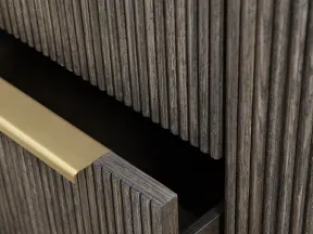 Close-up of a dark wood cabinet drawer with vertical grooves and a brushed gold handle partially open.