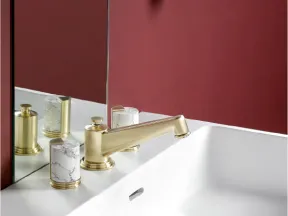 Modern bathroom sink with gold faucet, marble soap dispenser, and deep red wall with mirror reflection.
