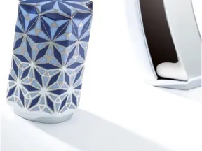 Blue and white geometric patterned vase with a star-shaped top next to a reflective metallic sculpture on white surface.