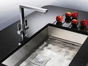 Modern stainless steel kitchen sink with black granite countertop and red apples on the side.