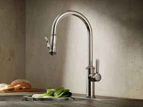 Sleek modern chrome kitchen faucet with high arch spout installed on wooden countertop near vegetables and bread.