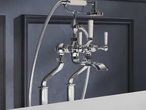 Polished chrome wall-mounted bathtub faucet with handheld shower and white ceramic handles on dark blue wall.