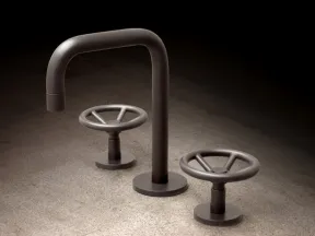 Modern industrial-style faucet with two round wheel handles on a concrete surface, lit with soft shadows.