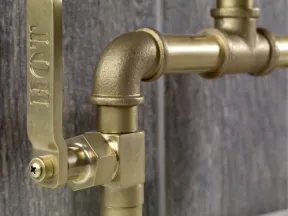 Close-up of a brass plumbing valve with a lever handle against a wooden background