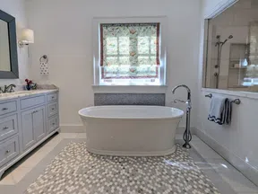 Modern bathroom with freestanding bathtub, patterned rug, gray vanity, and floral window shade.