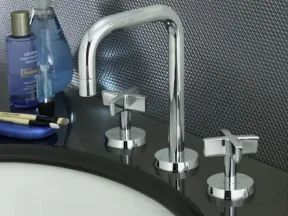 Modern chrome faucet with dual cross handles on a black countertop near skincare products and brushes