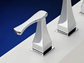 Modern chrome faucet handle with sleek geometric design on a white sink edge with deep blue background
