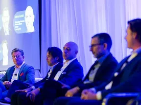 Panel of five professional men in suits engaged in a business conference with a presentation screen in background