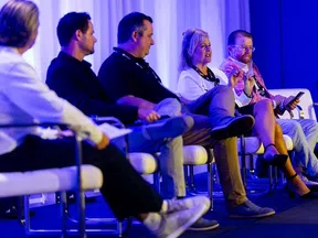 Panel of five professionals engaged in discussion on stage at a conference with blue lighting backdrop.