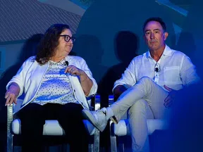 Two people seated on stage during a panel discussion, wearing microphones and listening attentively in blue lighting.