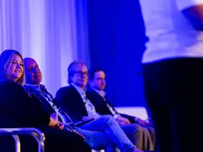 Panelists seated on stage during a conference with blue lighting and a speaker in foreground.