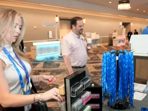 Woman selecting name badge while man holds coffee at conference registration table with blue lanyards.