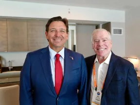 Two men in business attire smiling in a modern office setting with cabinets and a desk in the background