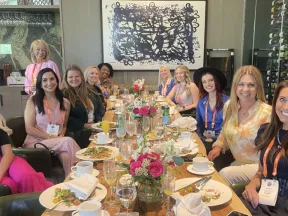 Group of women seated around a dining table with flowers and plates at a social event in a cozy restaurant.