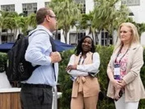 Three professionals in business attire conversing outdoors near a modern building with greenery and palm trees.
