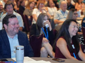 Audience of diverse professionals smiling and listening attentively at a conference or seminar event.