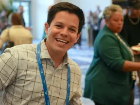 Smiling man in checkered shirt holding plate of food at a casual networking event or conference buffet.
