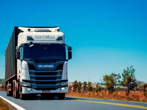 White Scania semi-truck with container driving on rural highway under clear blue sky