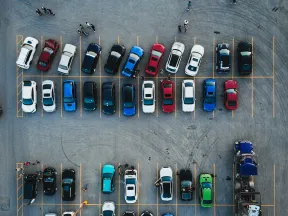 Aerial view of a parking lot with multiple cars in rows and people walking between the vehicles.