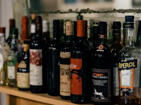 Assorted wine and liquor bottles lined up on a wooden shelf with varied labels and colors.