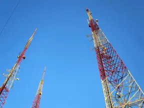 Three tall red and white communication towers with antennas against a clear blue sky.