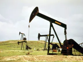 Multiple oil pumpjacks actively extracting crude oil on a grassy plain under a cloudy sky.