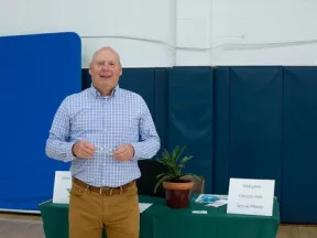Man in checkered shirt standing by table with plant and signs about websites, Google Ads, and social media.