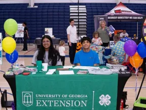 University of Georgia Extension table at community event with smiling volunteers, balloons, and promotional materials
