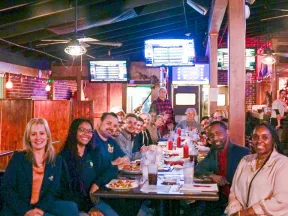 Group of diverse people enjoying a meal together at a restaurant with wooden decor and ceiling fans.