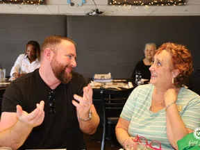 Man and woman engaged in friendly conversation at a cafe with people dining in the background.