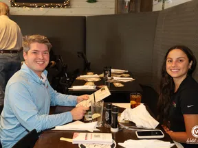 Two young adults smiling while seated at a restaurant table with menus and drinks, ready to order.