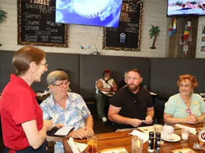 Group of four adults dining and conversing at a restaurant with seafood menu boards and TVs in background