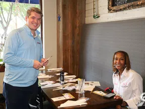 Man and woman smiling at a table with menus and papers inside a casual restaurant setting